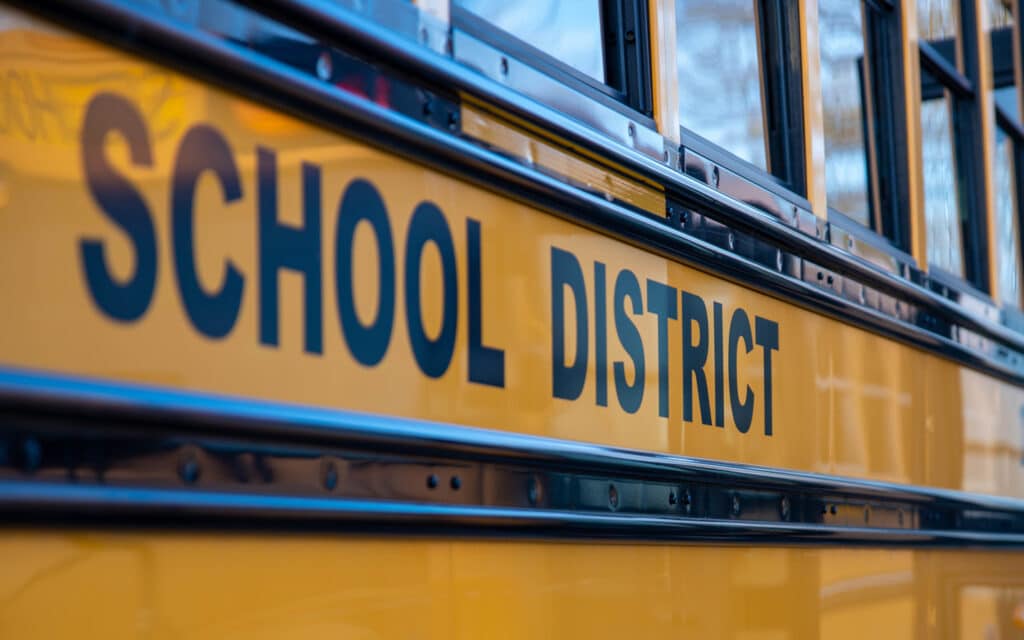 Close-up view of a yellow school bus with bold black lettering displaying "School District" on its side. The image highlights the distinctive color and signage typical of school buses, indicating affiliation with Clay County's educational system.