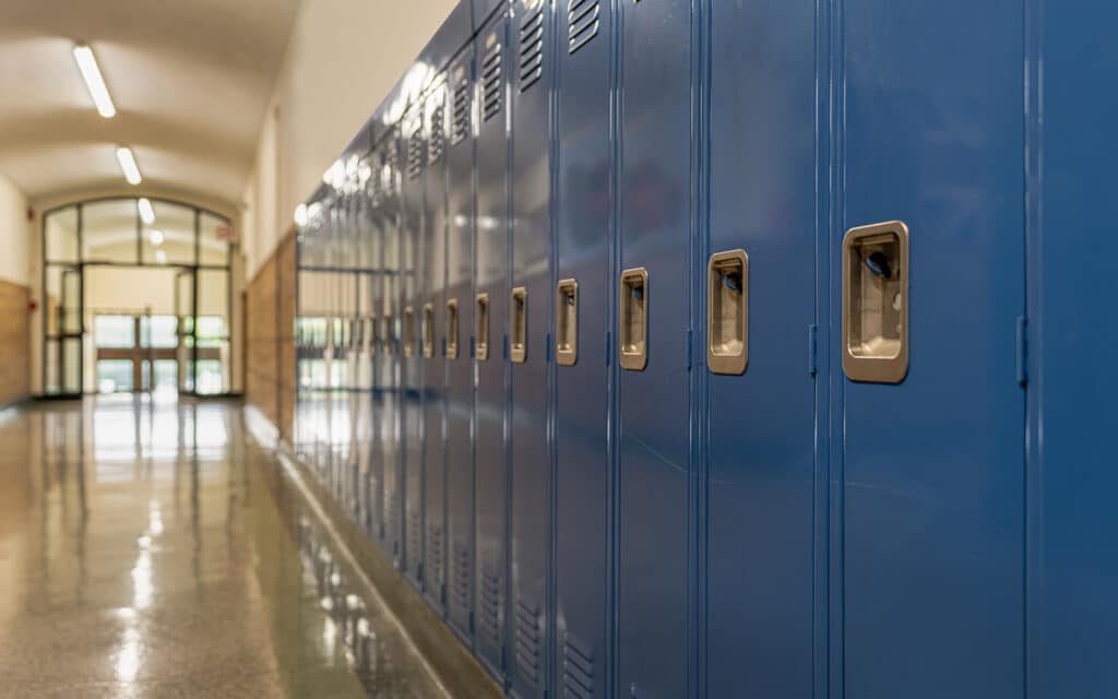 A row of blue lockers lines a polished school hallway, illuminated by fluorescent lights. The scene is prepared to welcome new students for their onboarding at Green Dot Public Schools, conveying an organized and inviting environment.