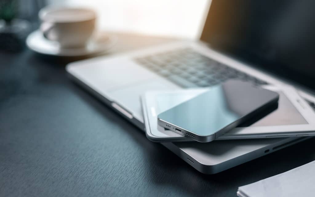 A smartphone and tablet are neatly stacked on a closed laptop, all placed on a wooden surface.