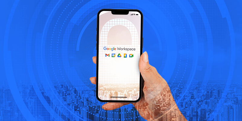 A hand holds a smartphone displaying the Google Workspace logo, surrounded by icons for Gmail, Meet, Calendar, Drive DLP, and Docs. In the background, cityscape silhouettes appear against a calm blue sky, adding an urban context to the technological theme.